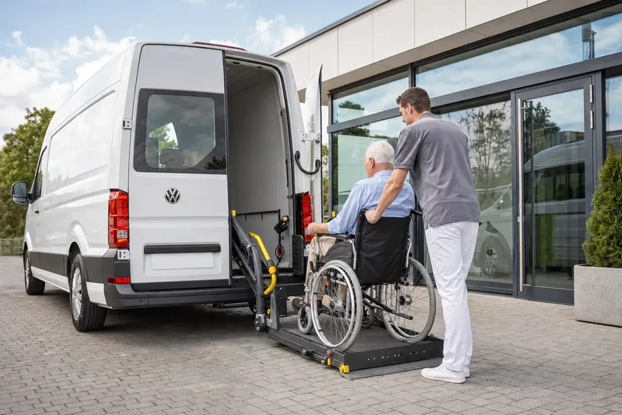 Rehabilitasyon merkezi önünde tekerlekli sandalyedeki yolcunun hidrolik liftle araca alınması